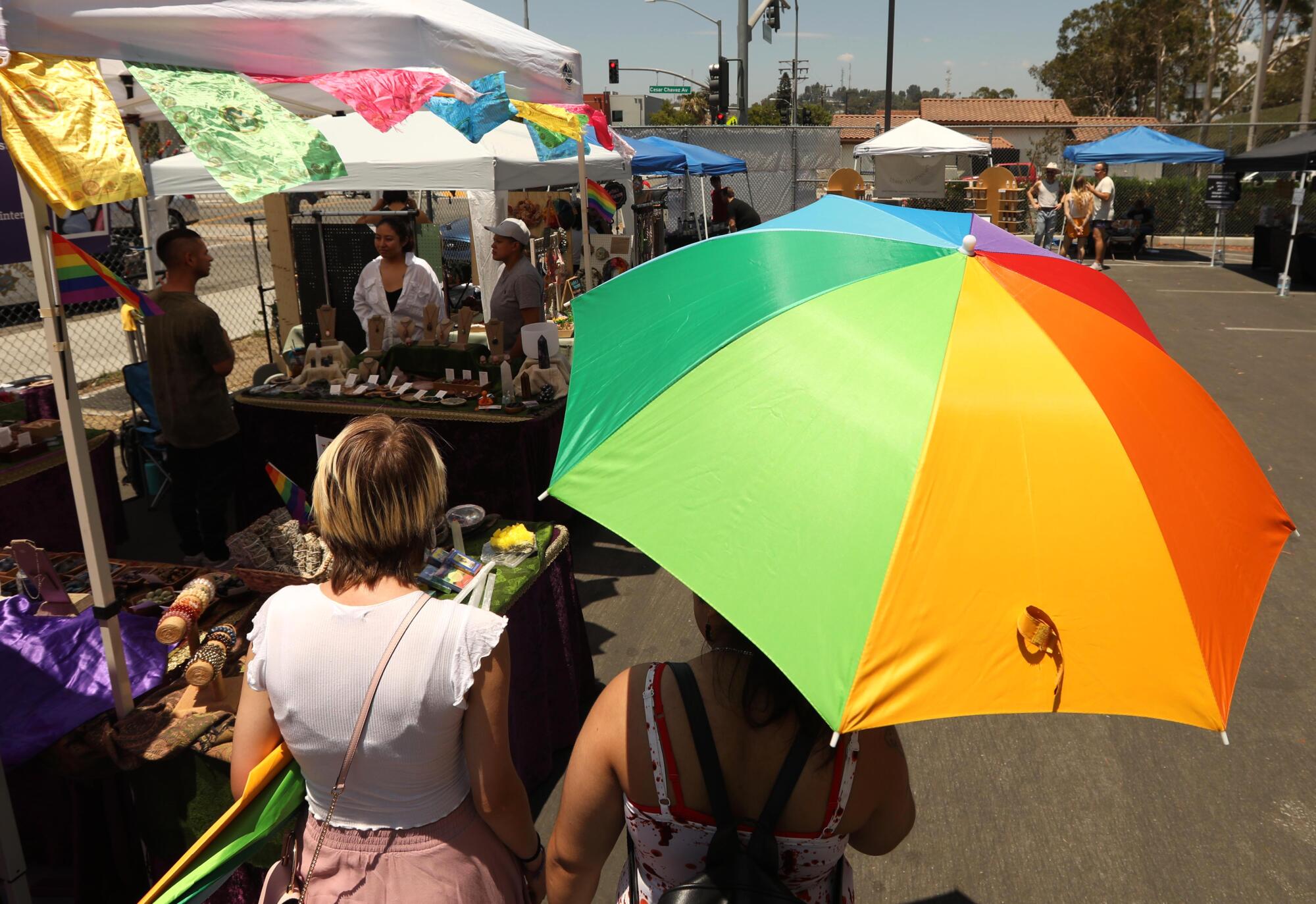 Shoppers, one carrying a LGBTQ pride umbrella, browse at the Queer Mercado.