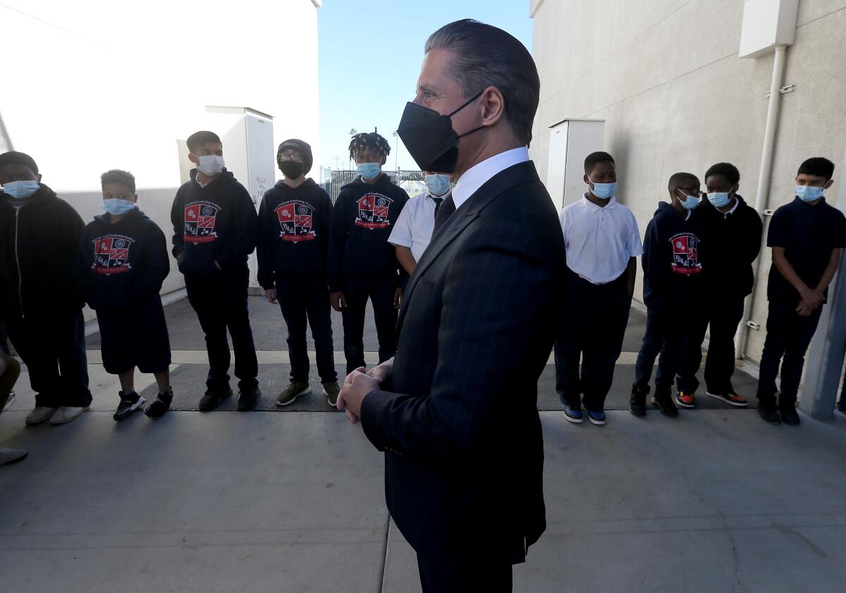 A man stands in front of boys in black pants and shirts or sweatshirts.