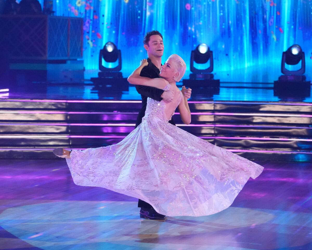 A man wearing dark clothing and a woman in a flowing pink dress dancing on a stage