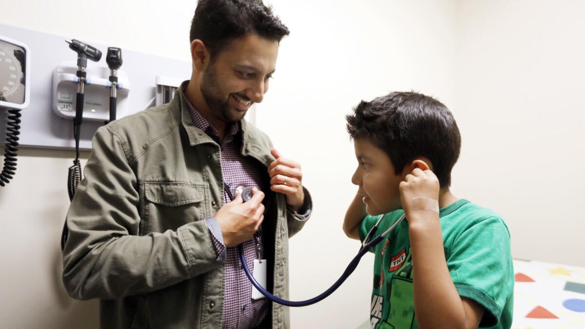 Dr. David Bolour allows Aaron Barba to listen to his heart during Aaron's physical exam at St. John's Wellness and Family Center.