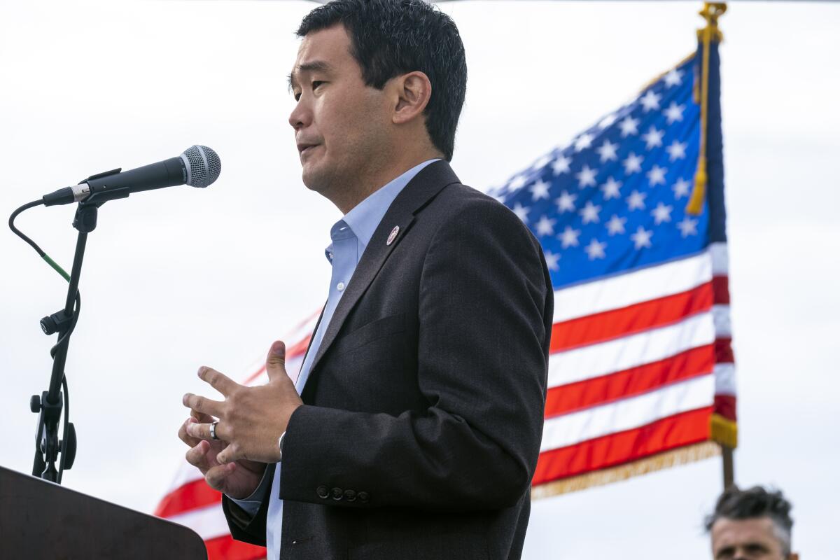 Dave Min speaks into a microphone in front of an American flag.