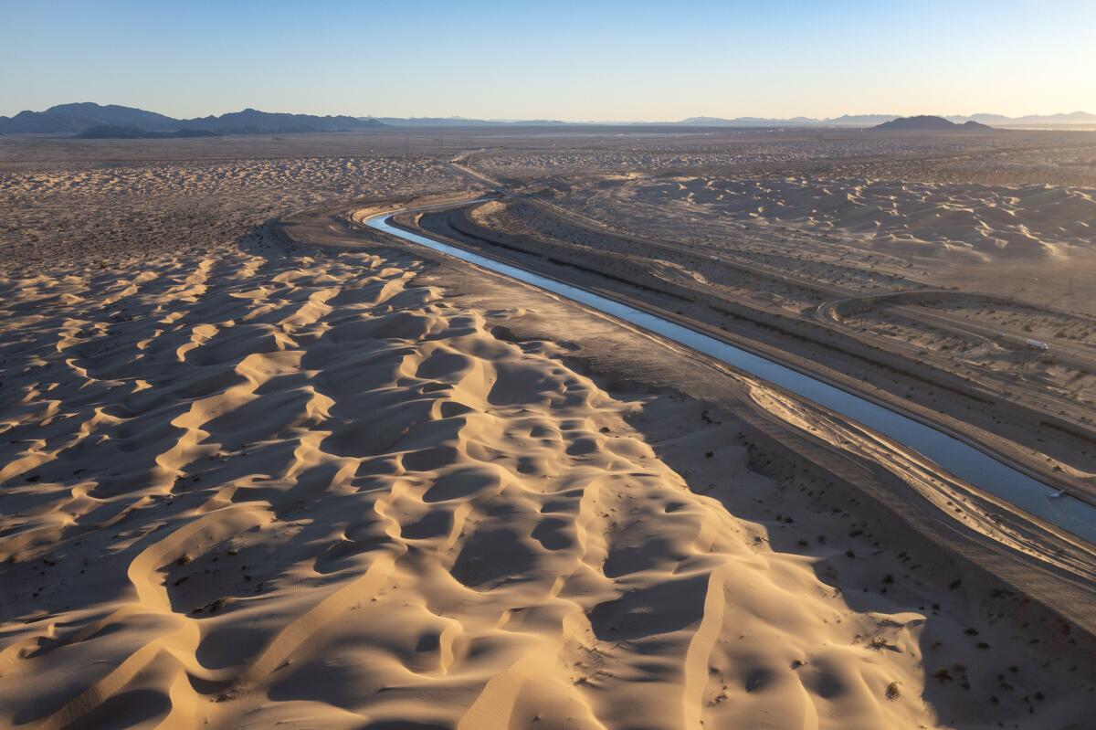 Sculpted sand dunes next to a canal that curls into the distance.