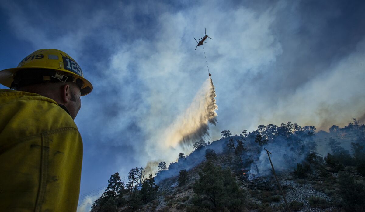 A firefighter looks up at a huge plume of water falling from a helicopter