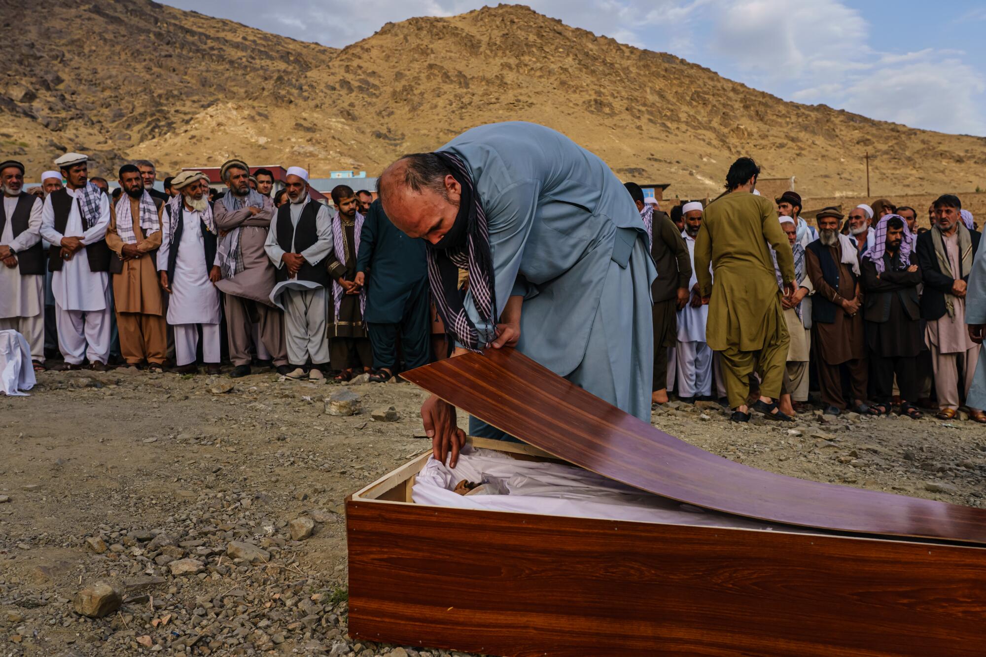 A man bids farewell to Zamari Ahmadi in his casket during Monday's mass funeral in Kabul. 
