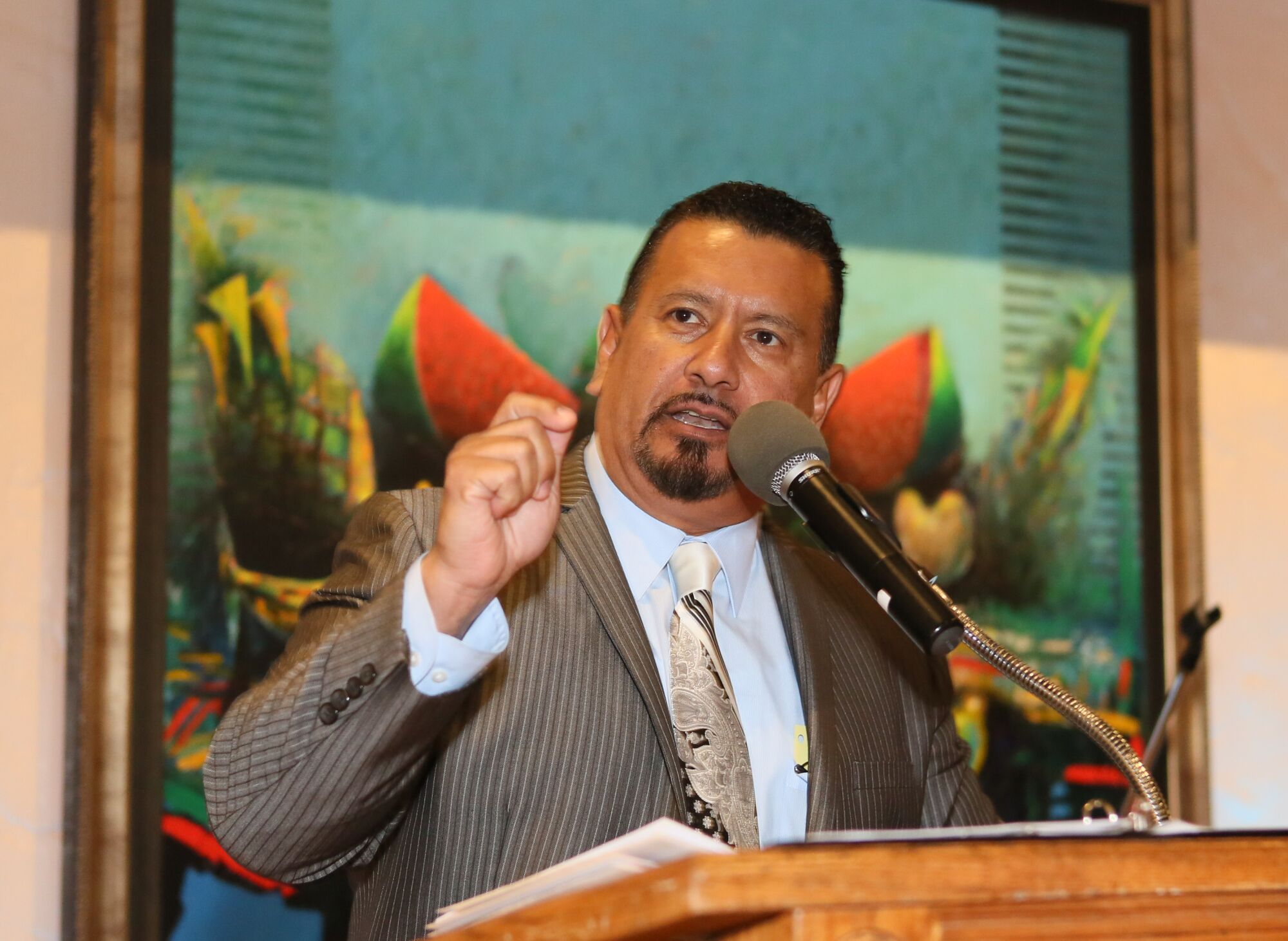 Richard Montañez speaks at a lectern in front of a painting
