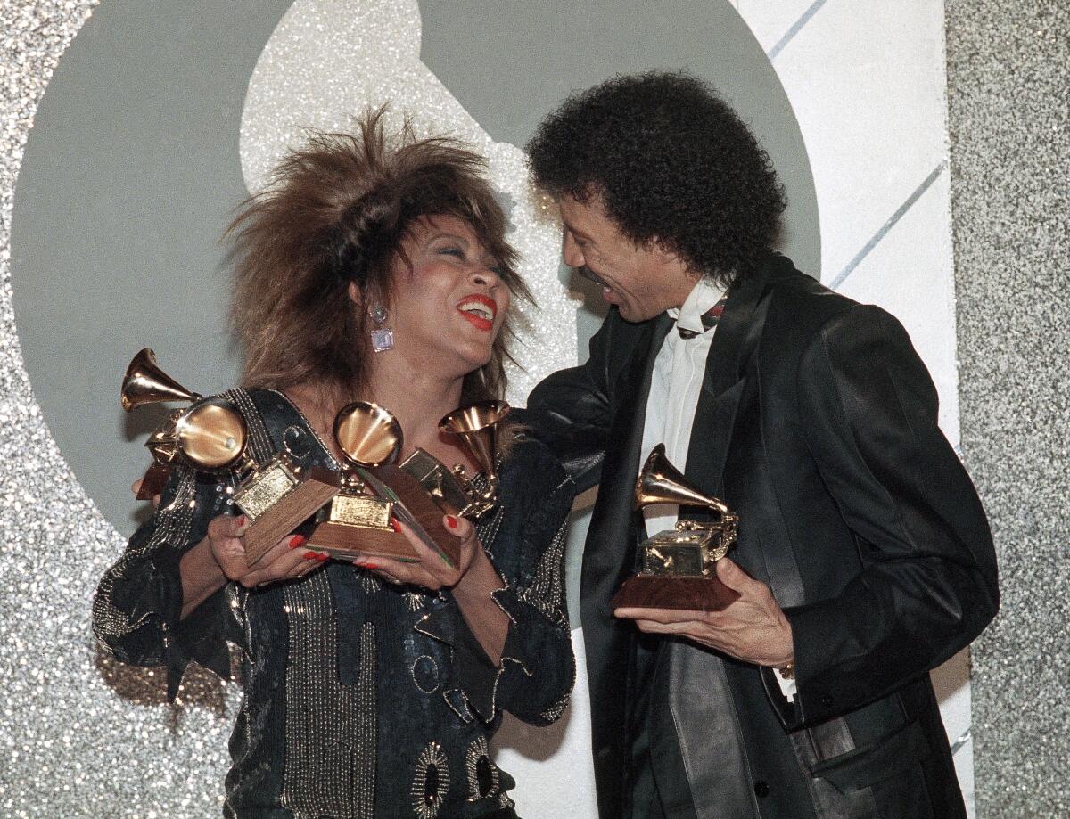 Tina Turner with Lionel Richie holding multiple grammys, smiling at each other 