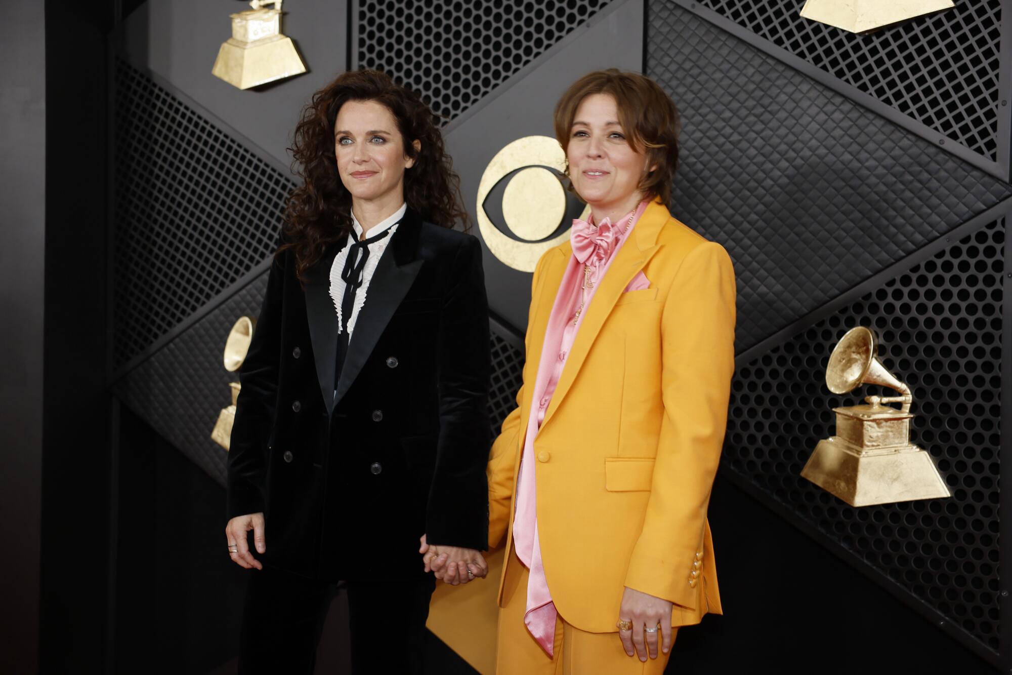 Catherine Shepherd in a black suit holds hands with Brandi Carlile in a yellow suit