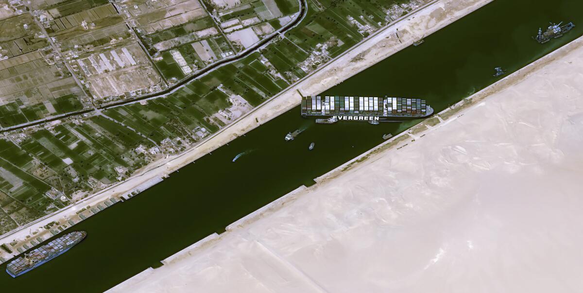 An overhead satellite image shows a container ship lodged sideways in a canal