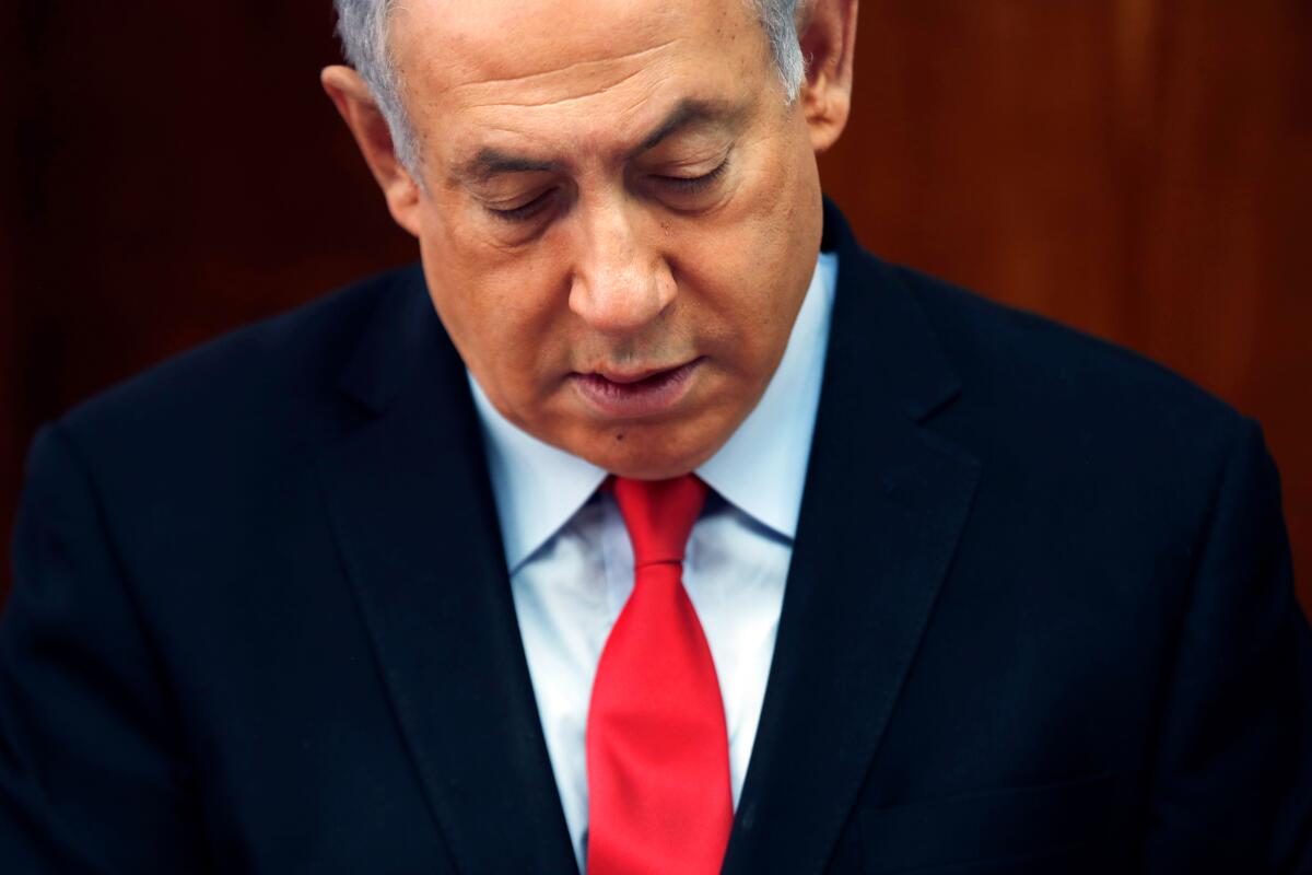 A close shot of Benjamin Netanyahu in a suit and red tie, looking down