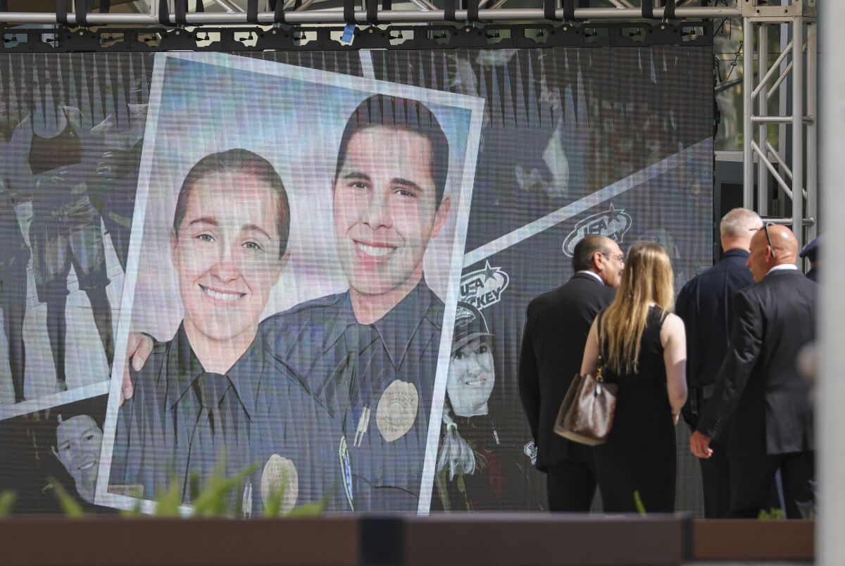 Mourners walk near photos of deceased SDPD Detectives Jamie Huntley-Park and Ryan Park at Maranatha Chapel on June 15
