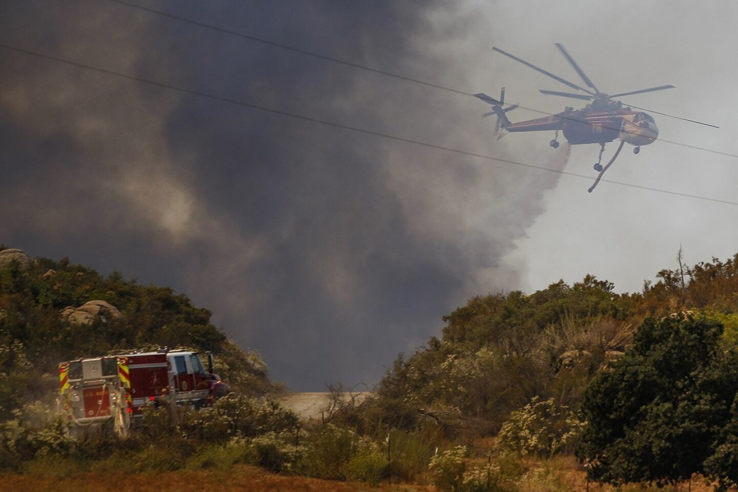 A helicopter drops water on a wildfire burning close to Highway 94 near Potrero on Monday.