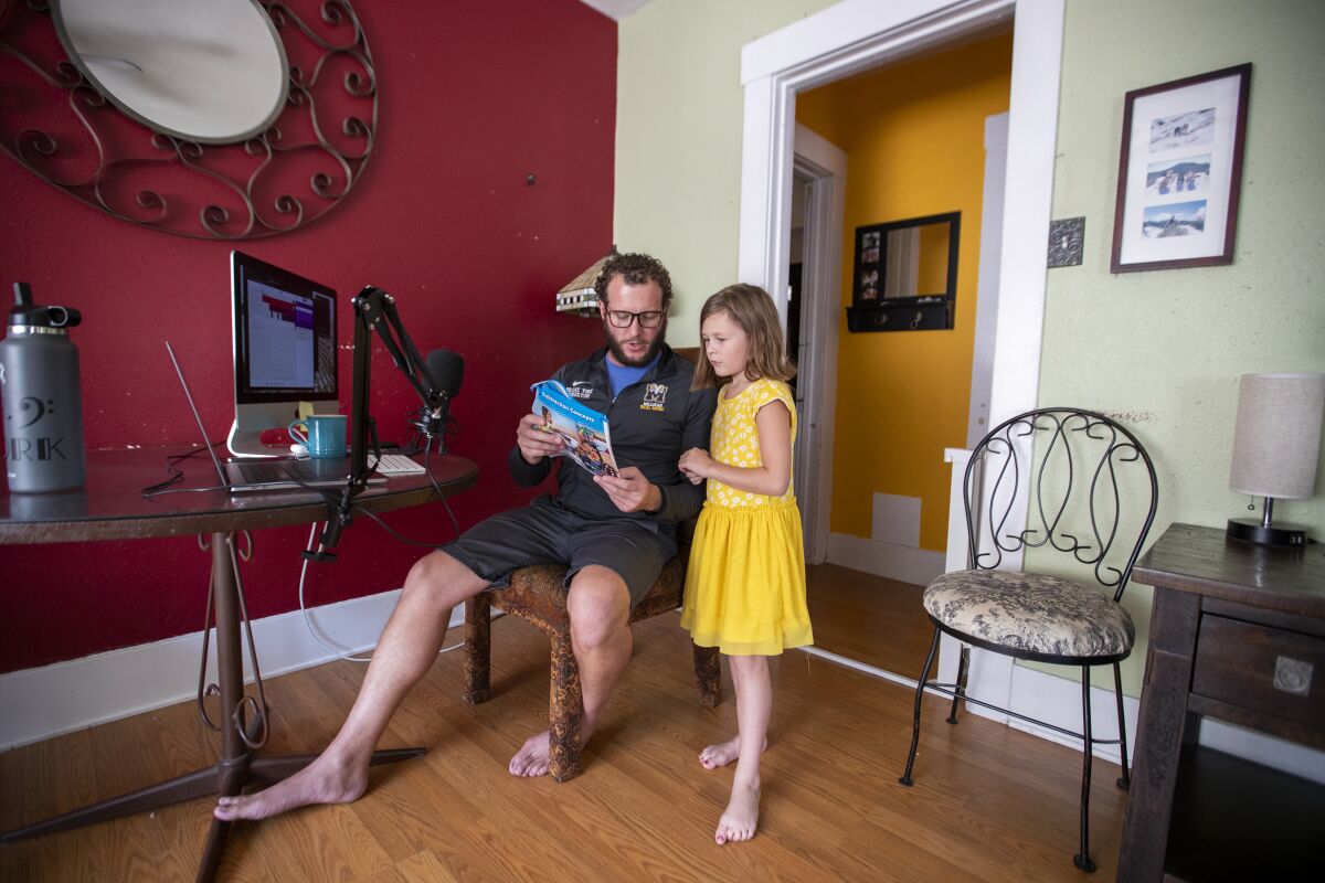 A child and her father read a book in front of their computer in a home.