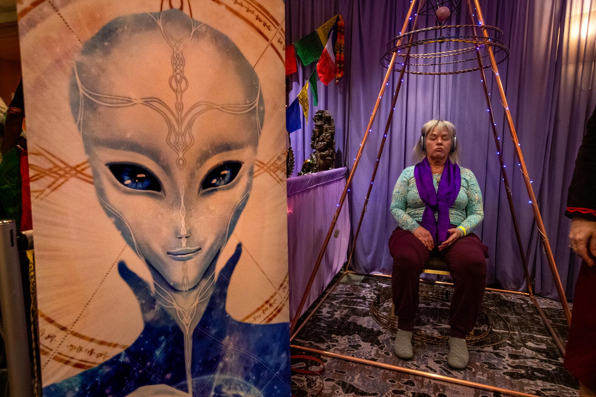 Carol Chappell, from Sedona, Ariz., sits inside a pyramidal structure next to a large drawing of an alien