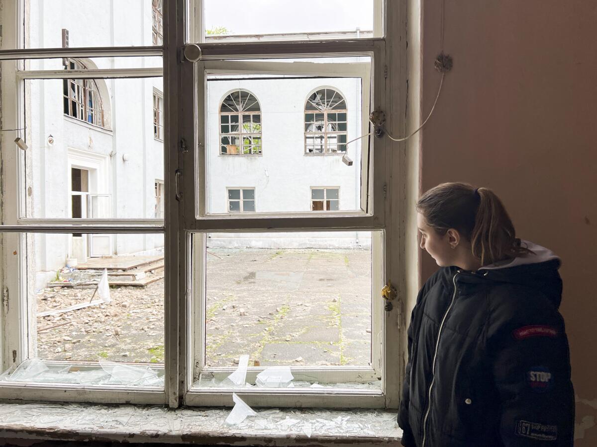 A woman looks out of broken windows.