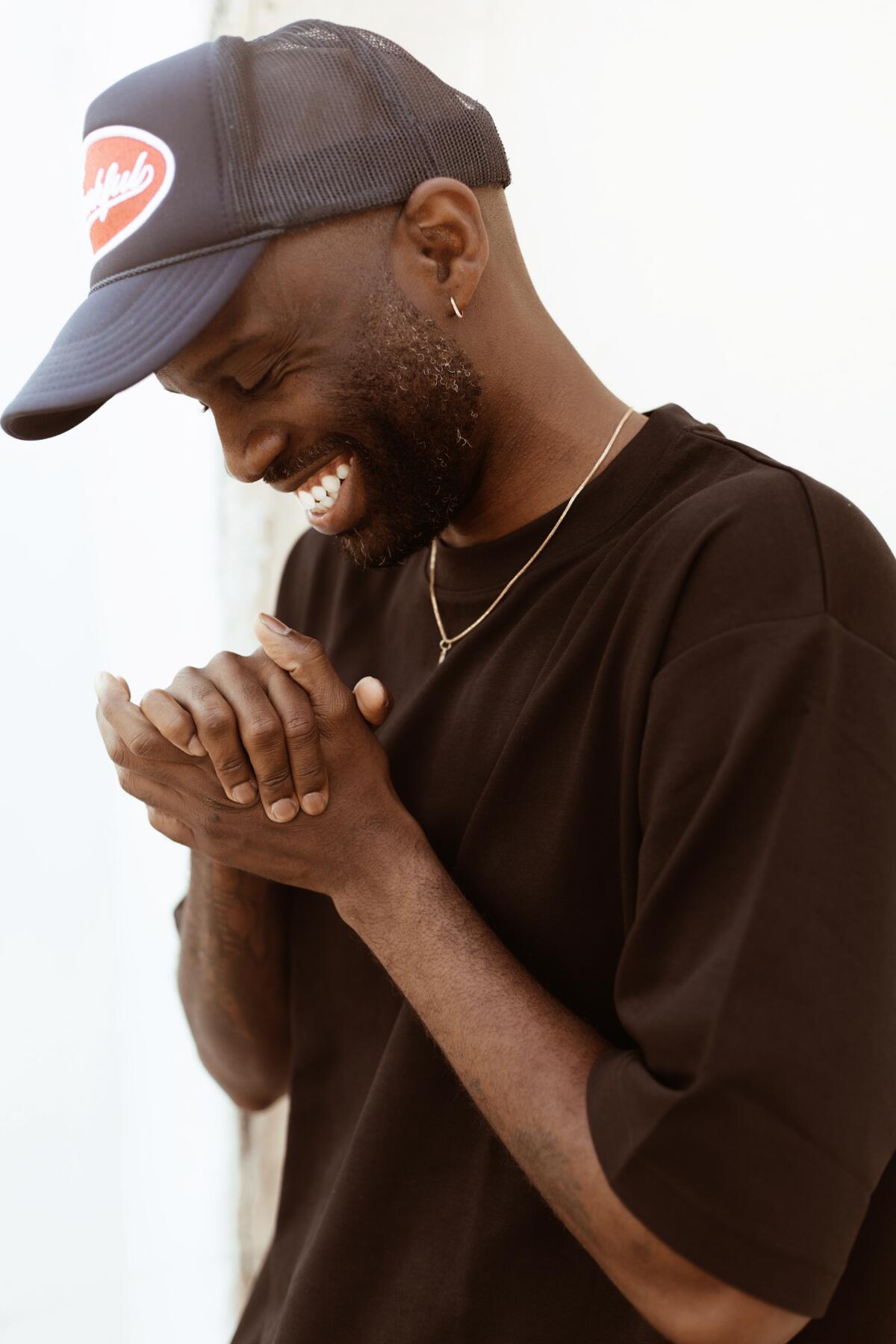 Black man iin trucker hat smiling with hands folded