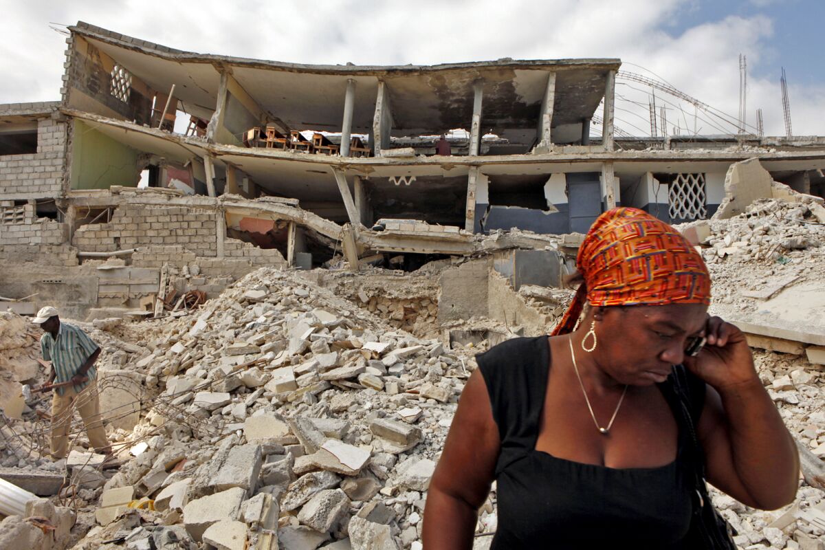 Two people stand amid piles of broken concrete and a collapsed building