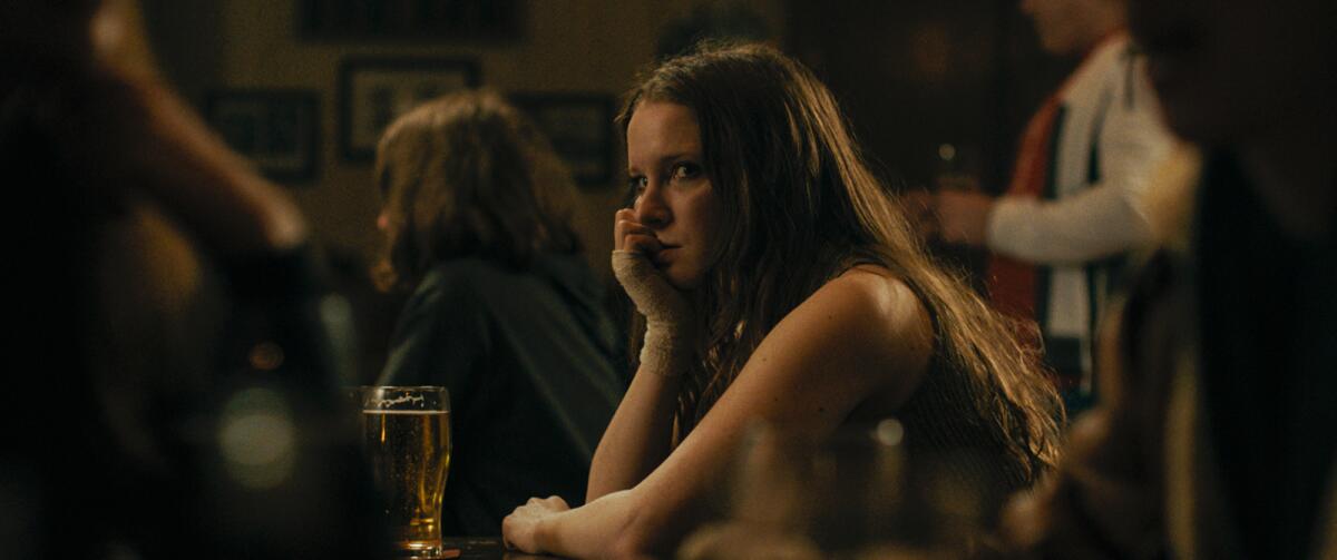 A woman sits at a bar with a pint of beer in front of her.