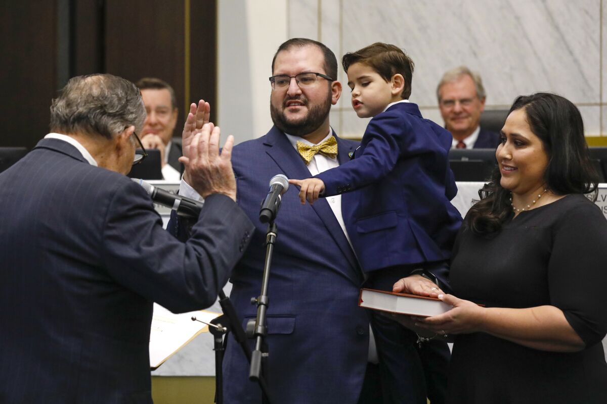 A man in a bow tie holding a little boy is sworn into office, his hand raised to take an oath.