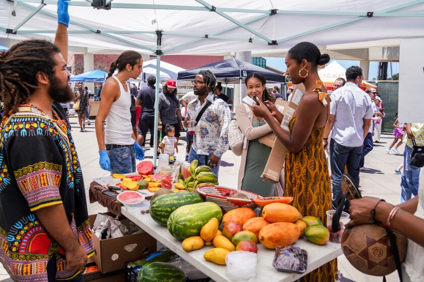 A small group of shoppers and vendors gathers around a table of produce at one of Prosperity Market's farmers market events.