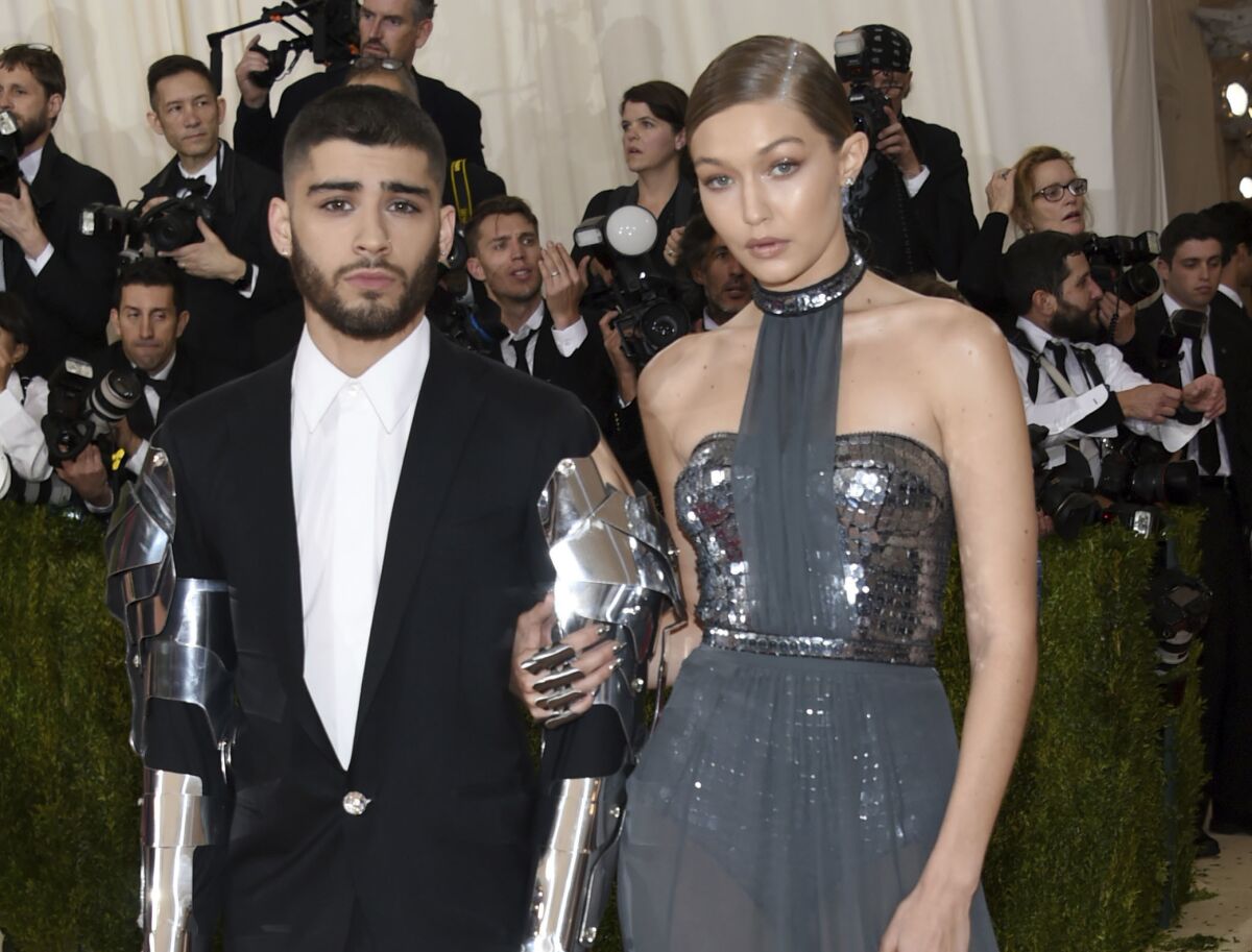 A man in a dark suit with metallic arms poses with a woman in a metallic dress