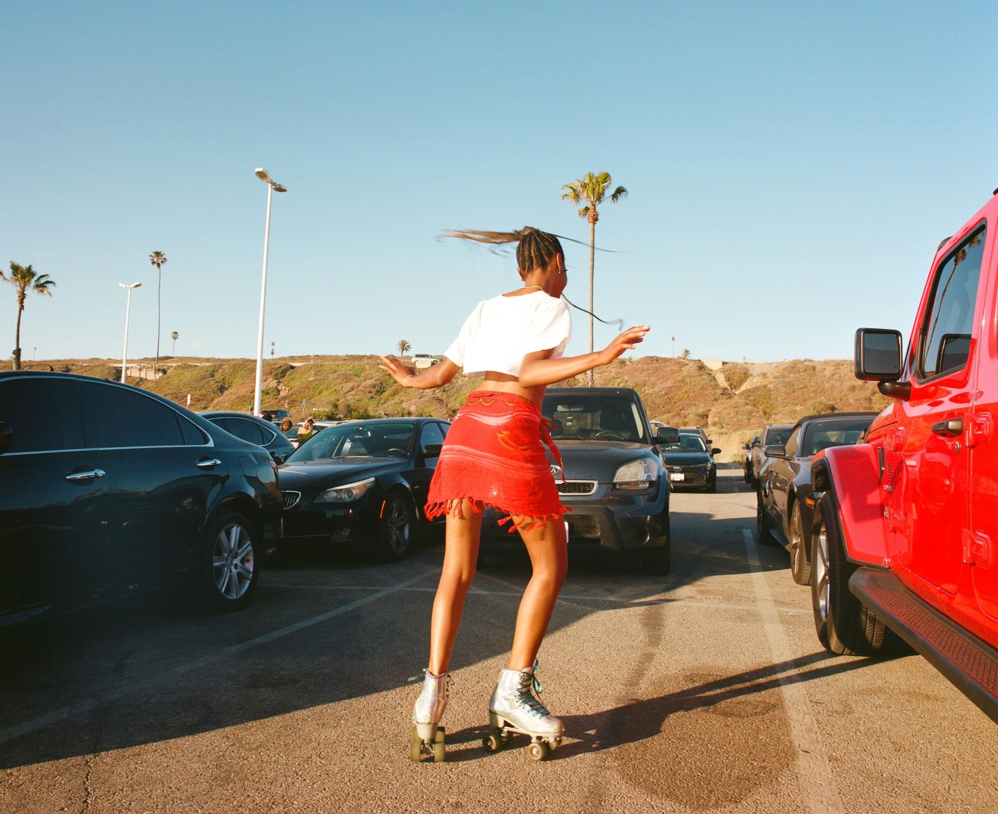 A woman in a red skirt and white crop top roller blades in a beach parking lot 
