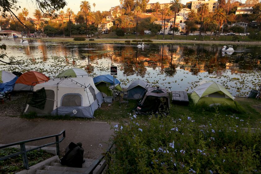 A homeless encampment on the banks of Echo Park Lake sits in shadow as the sun illuminates the water