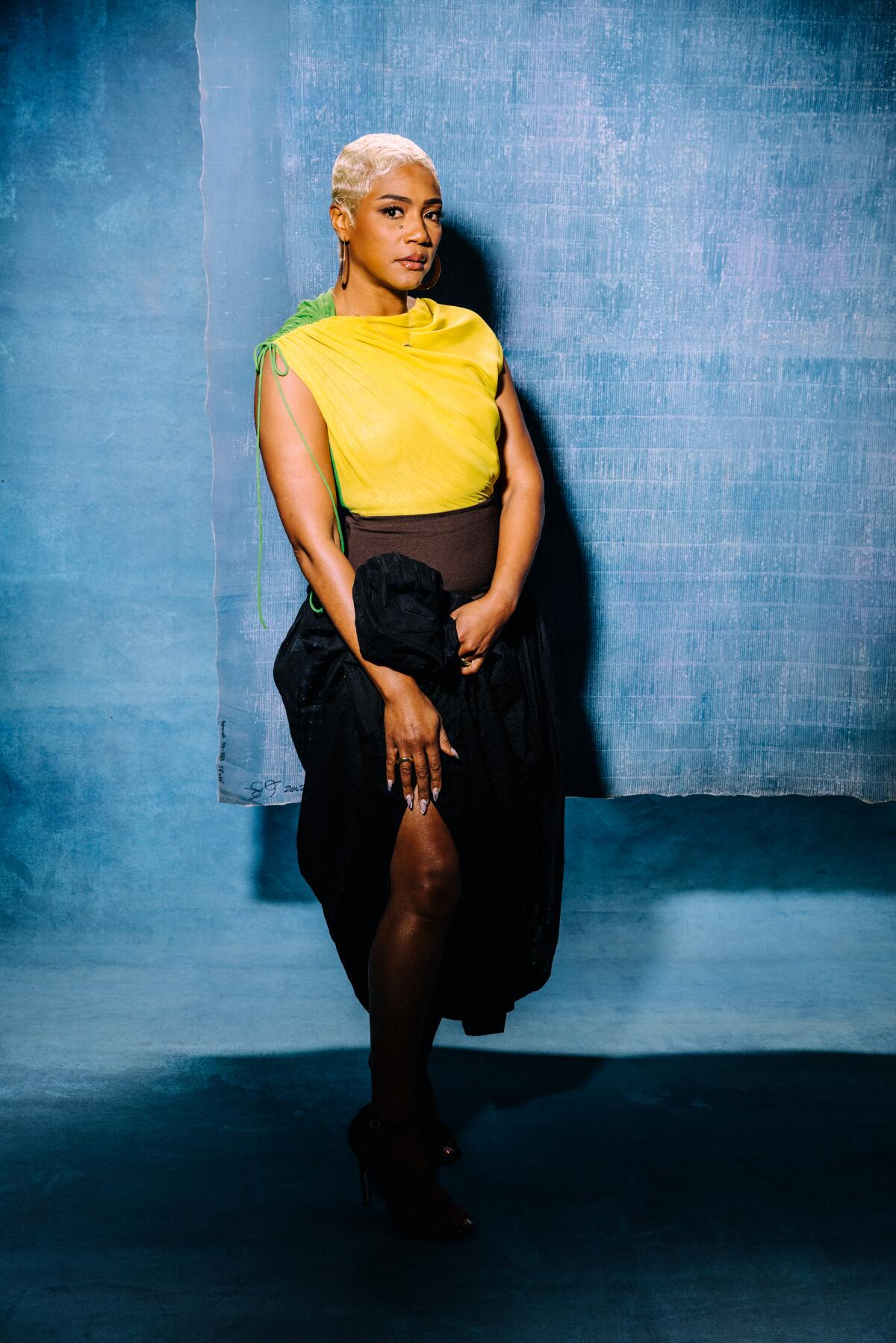 Black woman with close cropped blond hair standing against blue backdrop