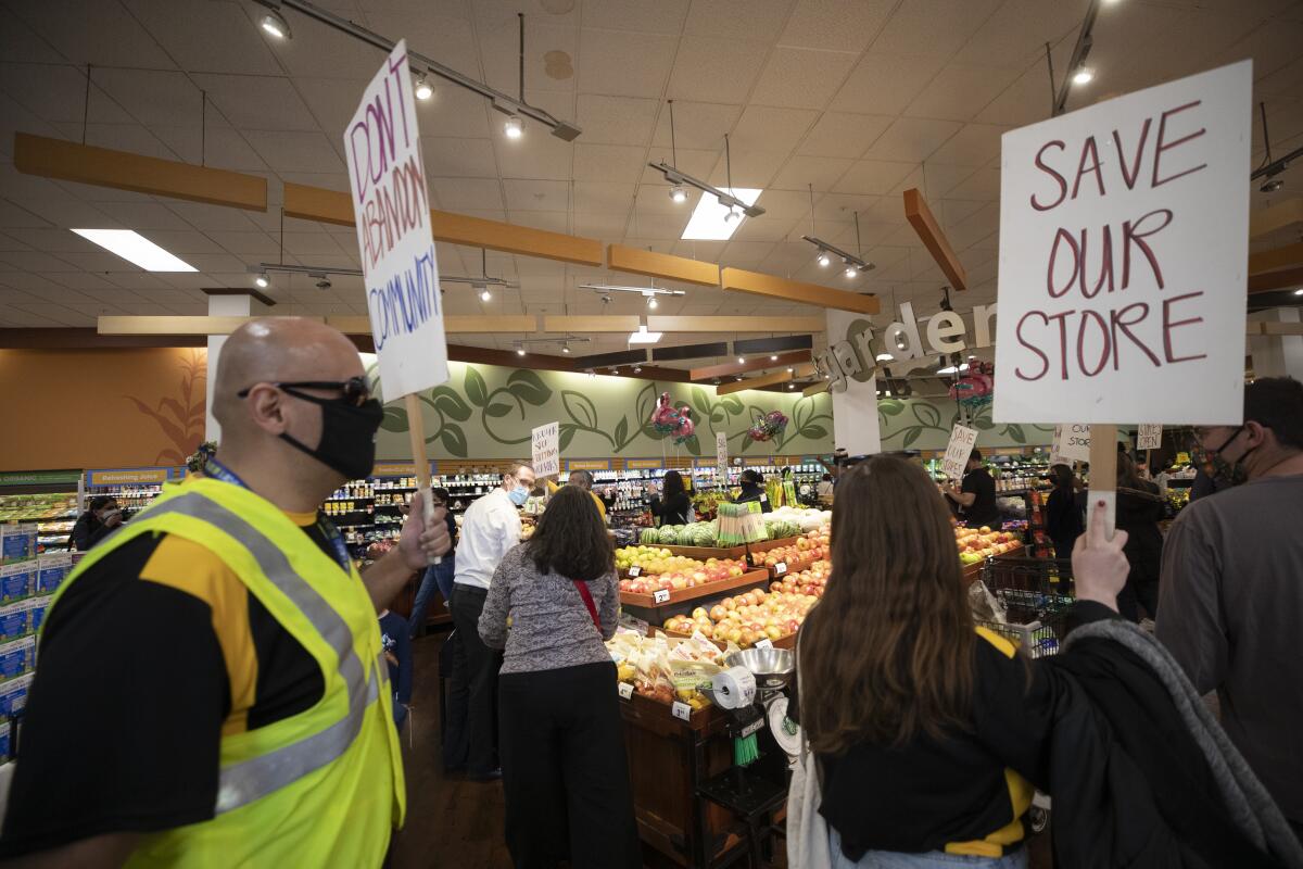 Protesters in a supermarket with signs that say Don't Abandon Community and Save Our Store