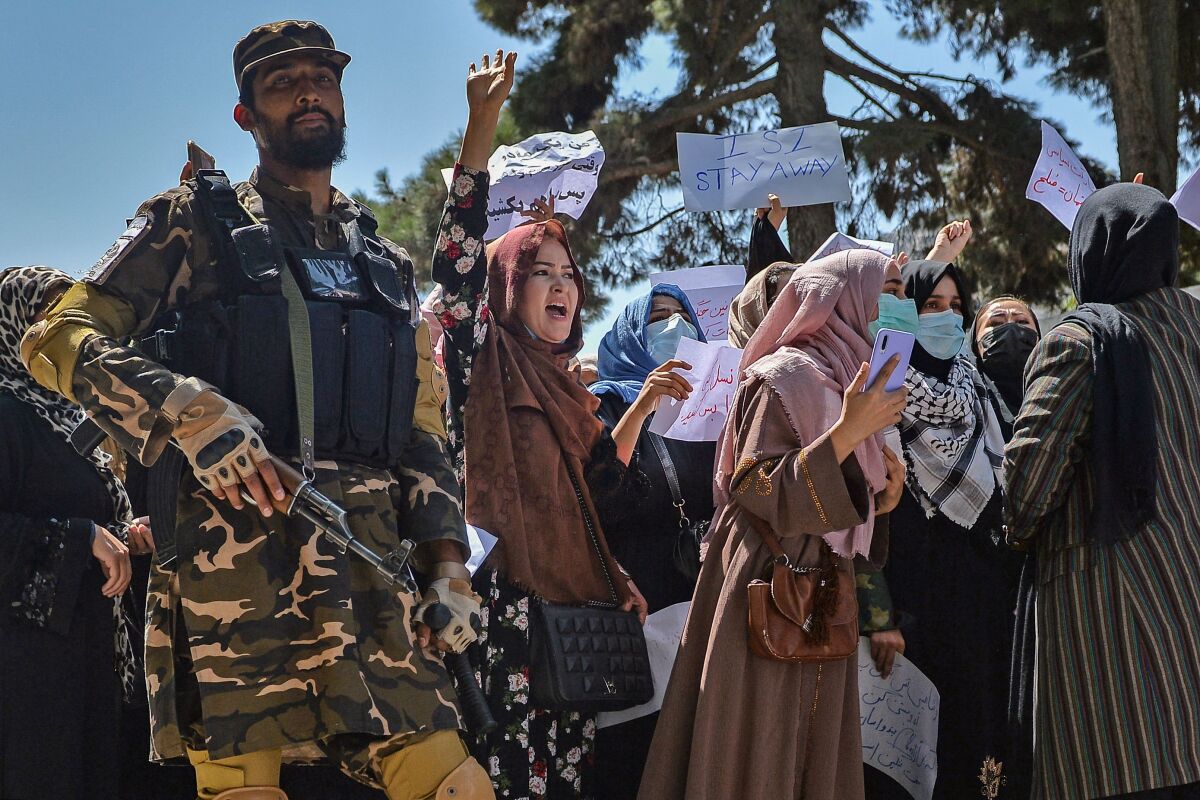 A Taliban fighter stands guard as Afghan women shout slogans 