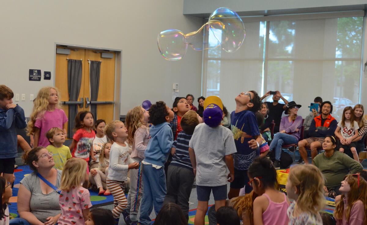 Kids try to blow the giant bubble upward during the bubble show Saturday at Mariners library.