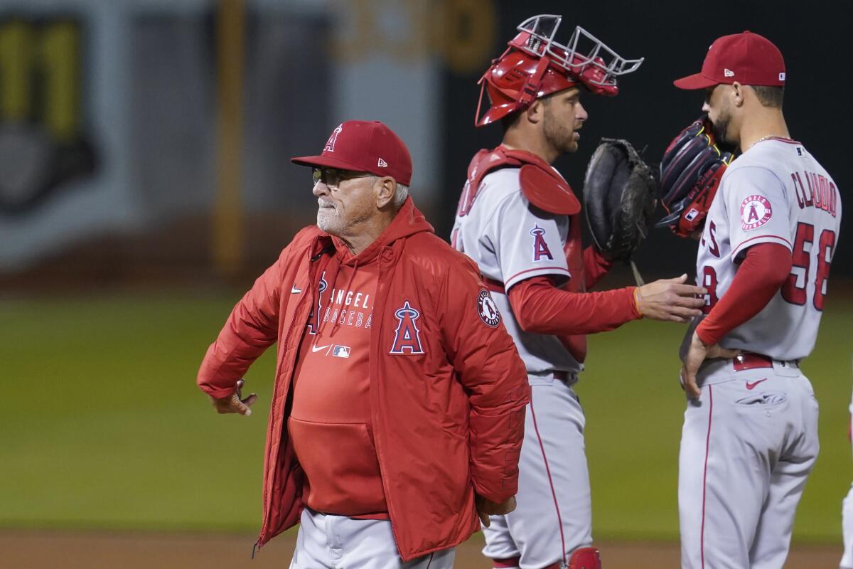 Angels manager Joe Maddon, left, walks off the mound in front of catcher Drew Butera, middle, and pitcher Alex Claudio.