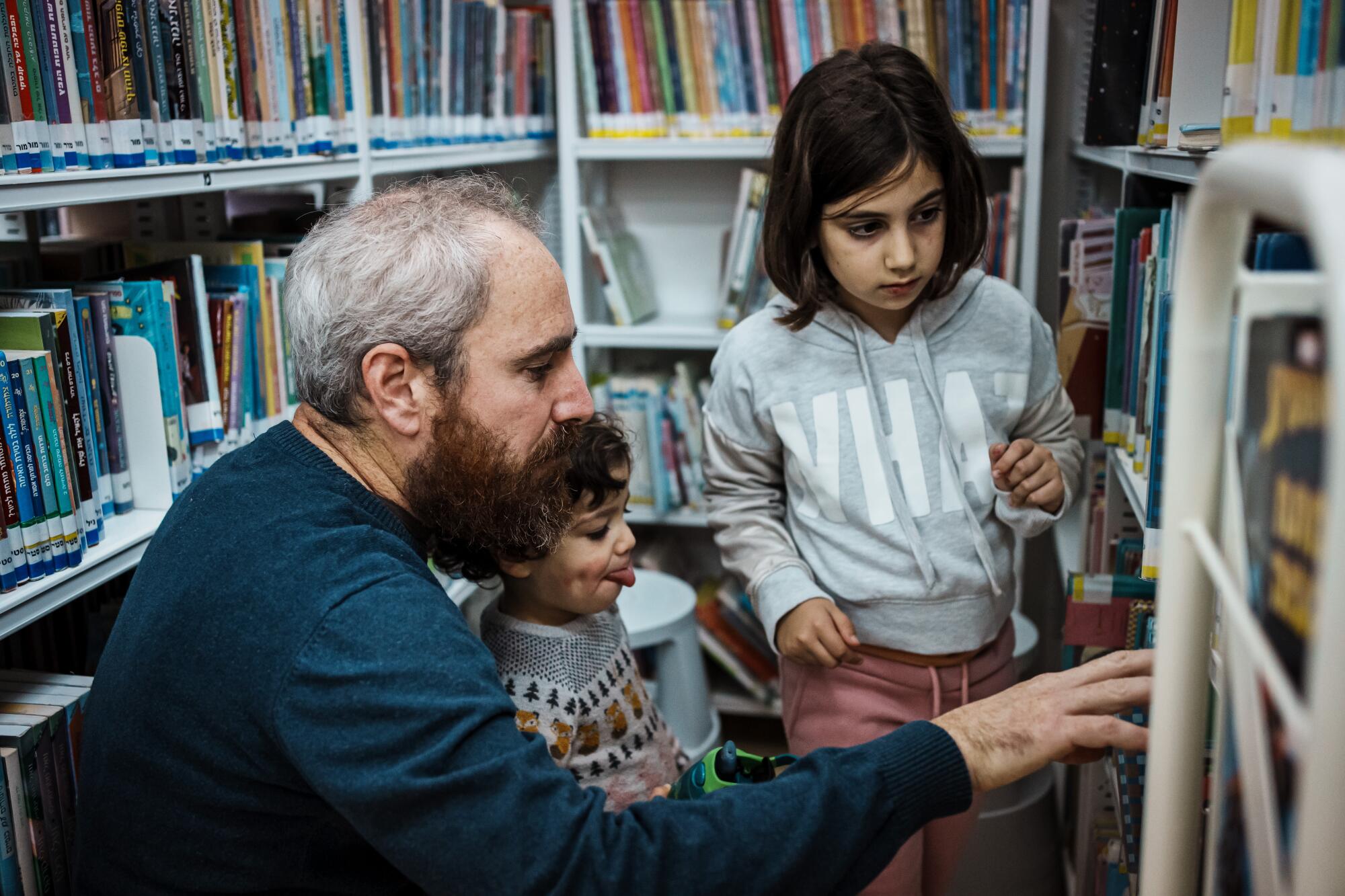 A man and two children look at books on shelves