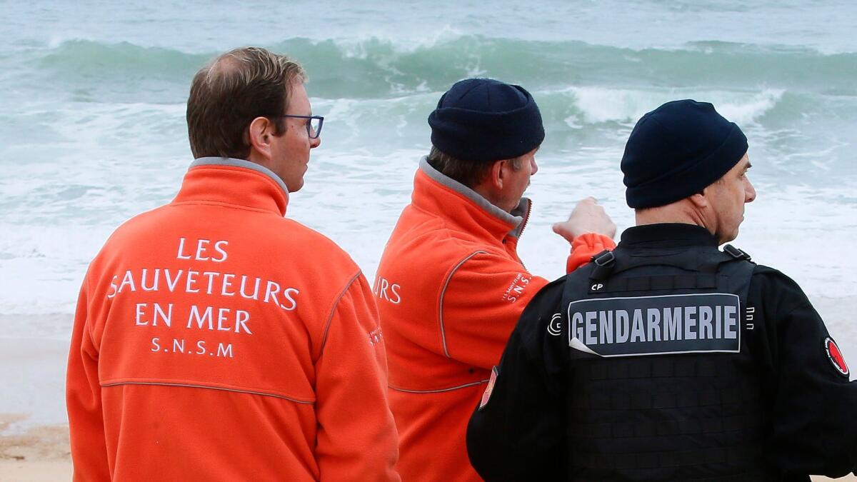 A French gendarme, right, and rescue workers chat during searches for Quiksilver's CEO on the beach of Hossegor, southwestern France, on Jan.31, 2018.