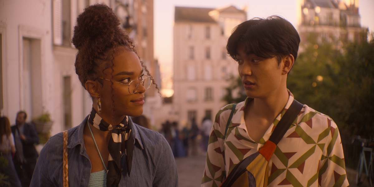 A young woman looks at a young man as they walk down a street.