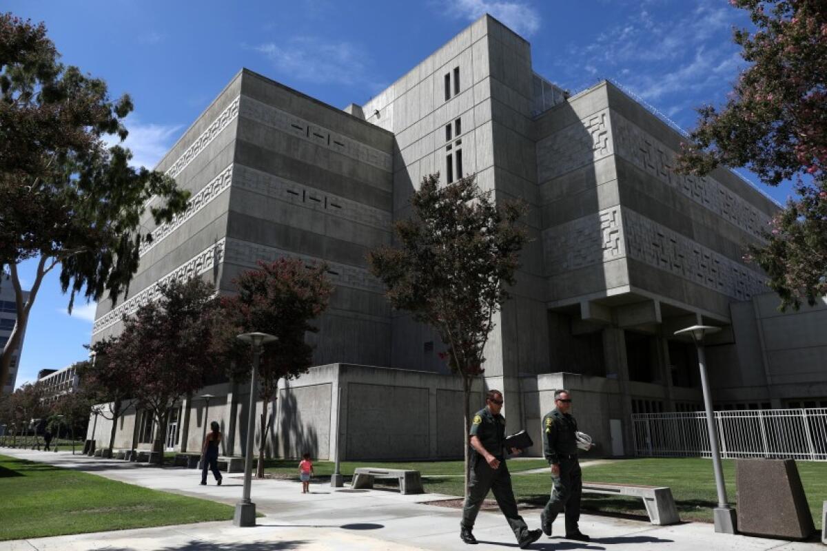 Two deputies in uniform walk on a sidewalk outside the Orange County Jail building