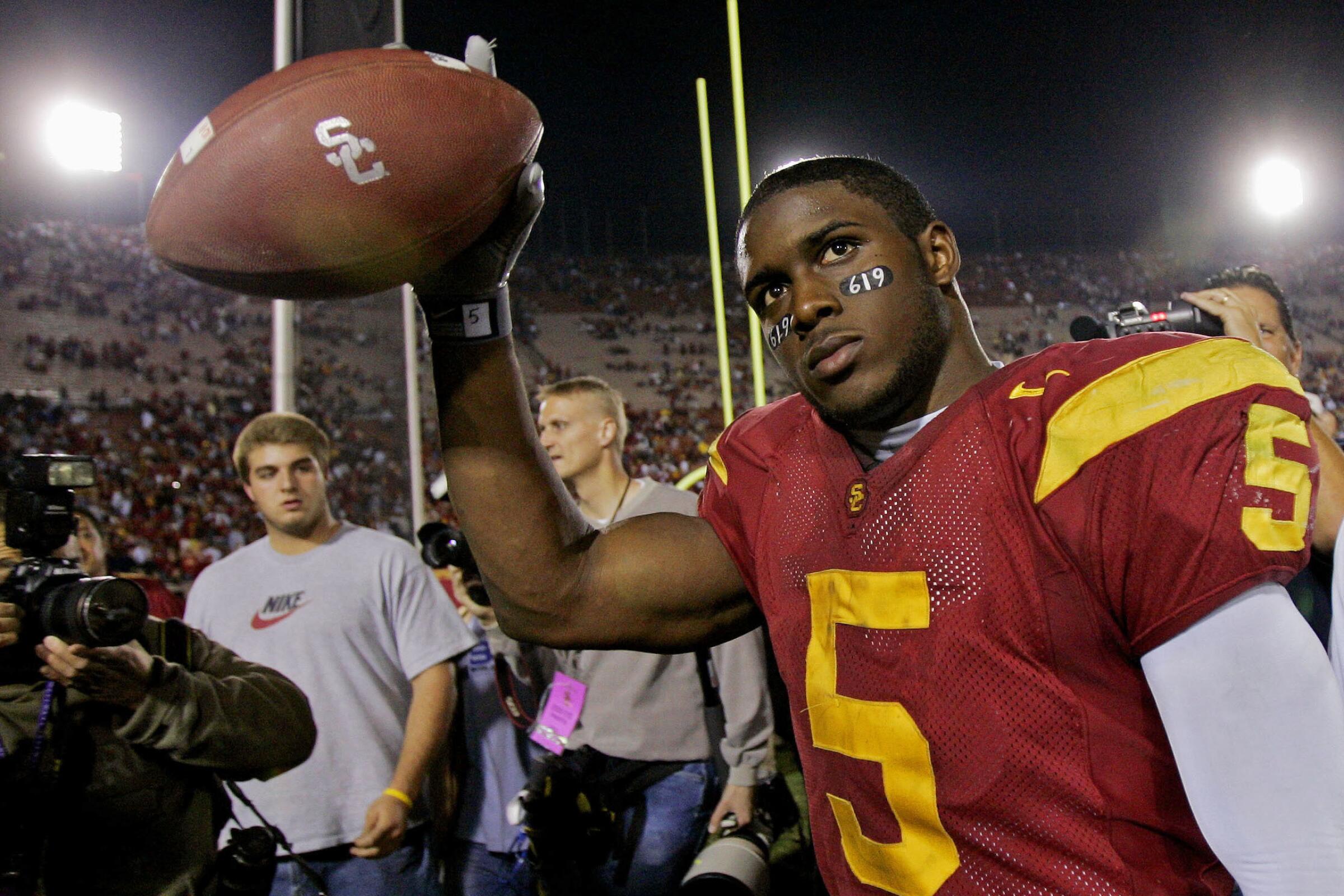 Reggie Bush holds up a football on the field next to a TV camera