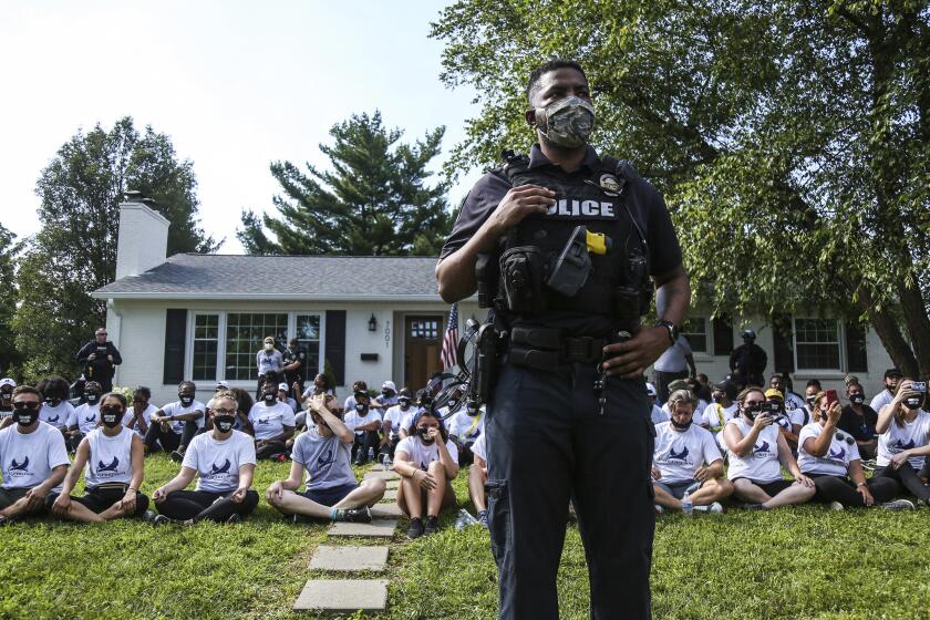 In this image from video, a Louisville Metro Police Department office stands guard outside the home of Kentucky Attorney General Daniel Cameron as protestors sit in his front yard in Louisville, Kentucky Tuesday, July 14, 2020. About two dozen protestors were arrested. Protesters were chanting Breonna Taylor's name as well as calling for justice after the 26-year-old emergency room technician was fatally shot by LMPD in her South End Apartment while police were serving a search warrant. Cameron said he still has no timeline for when his office will conclude its investigation of the case. (Mary Ann Gerth/Courier Journal via AP)