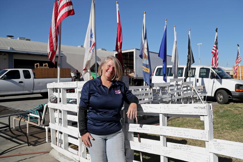 Owner Penny c stands next to the Burden and Regrets wall, a white picket fence where veterans leave messages, at Patriots and Paws in Anaheim. Lambright spent her entire 150K inheritance on starting a nonprofit to help veterans, who show up throughout the day to pick up all manner of home furnishings.