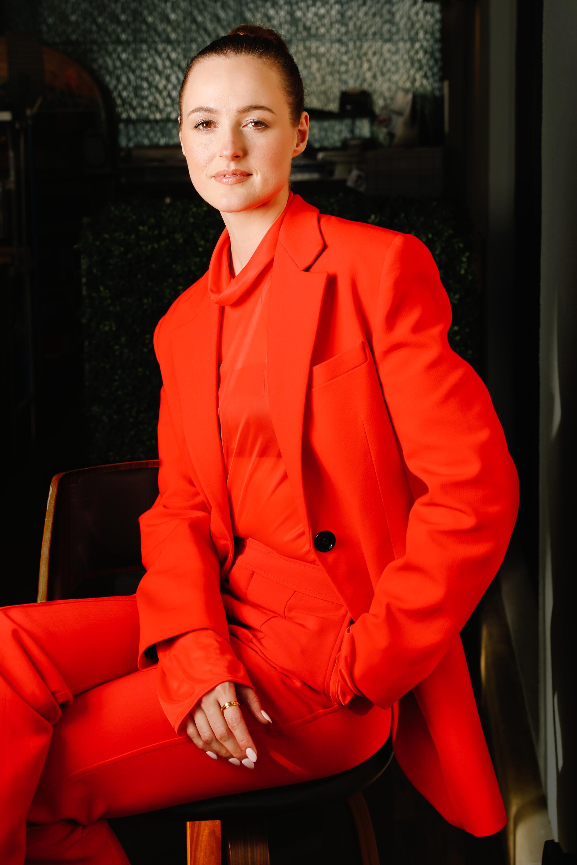A seated woman poses in a red suit.