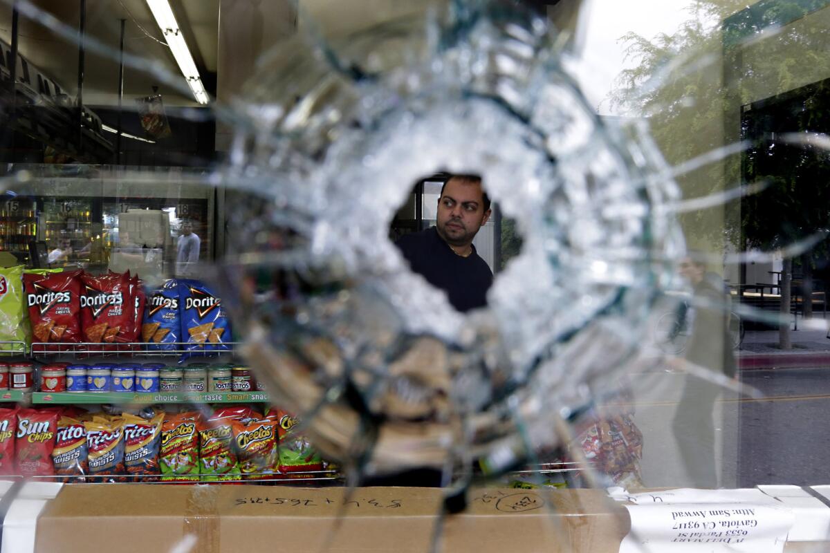 Seen through a bullet hole, IV Deli Mart owner Michael Hassan cleans up his store near UC Santa Barbara. A gunman fatally shot someone there.