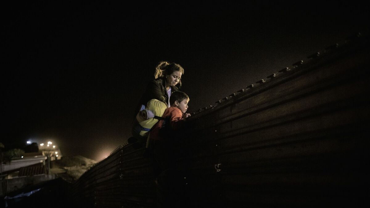 A migrant family from Honduras climbs the border fence to jump inside the United States to San Diego, from Tijuana, Mexico, Wednesday, Dec. 26, 2018.