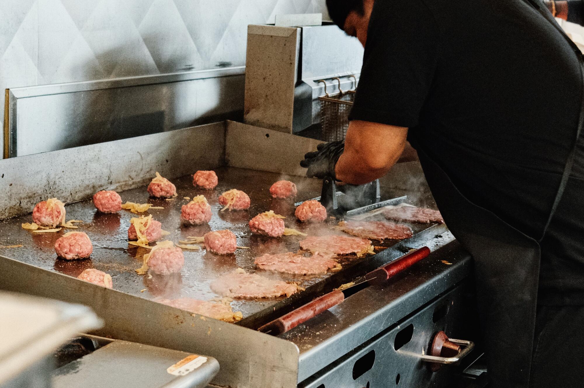 An employee crushes Wagyu Beef Patties on the grill in Marathon Burger in Melrose Avenue.