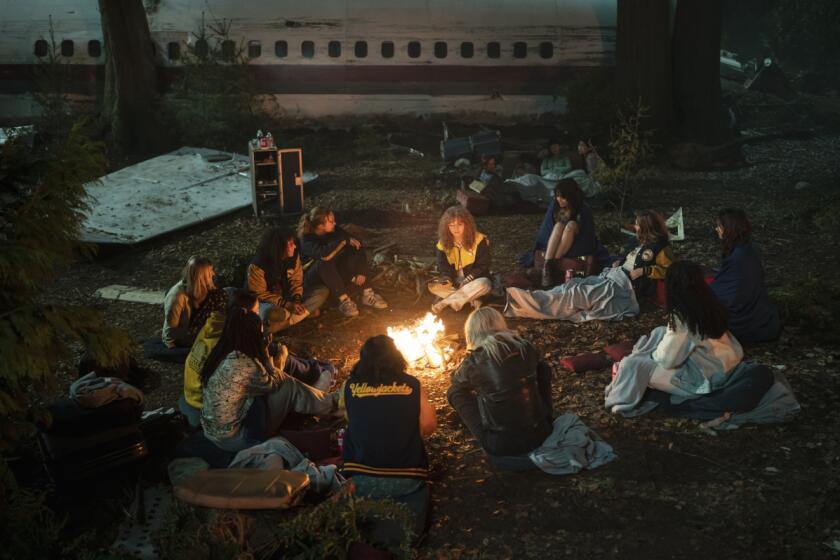 The teenage survivors of a plane crash sit around a fire in the wilderness