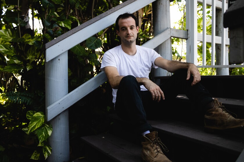 A man in a white T-shirt sits on the steps of a porch.