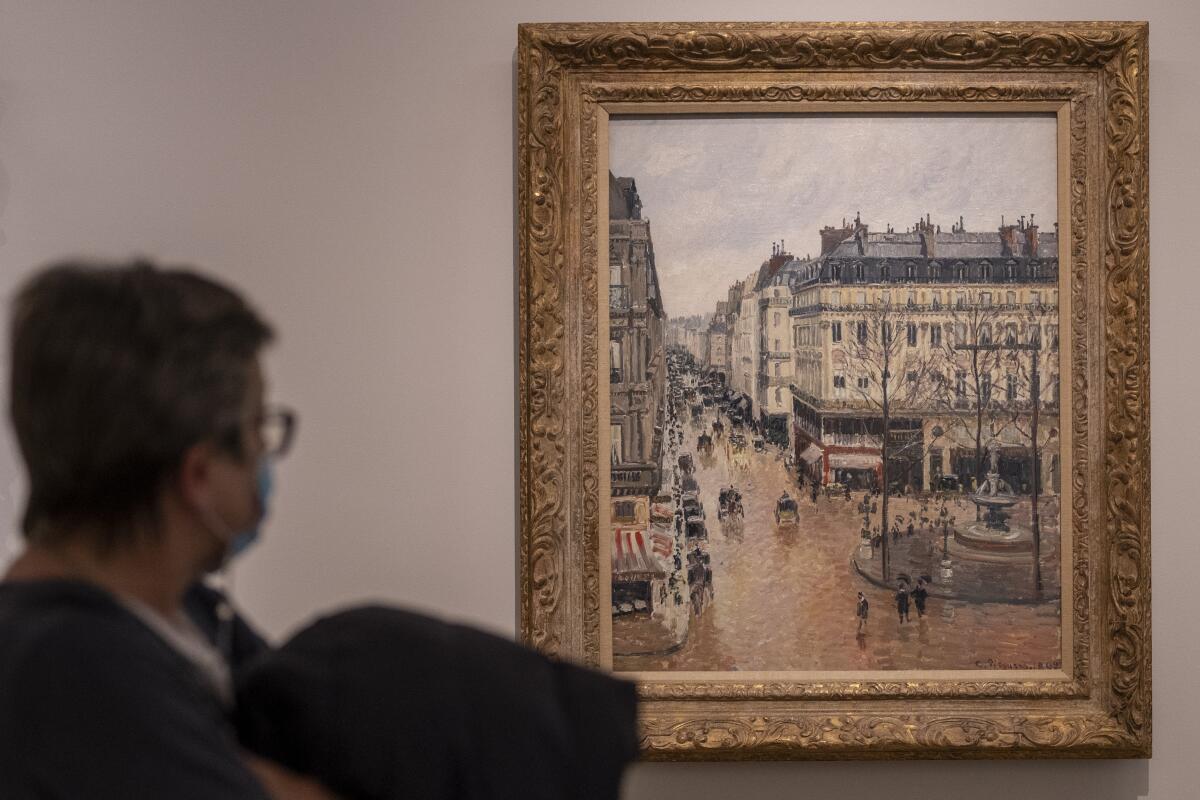 A woman looks at a painting called "Rue St.-Honore, Apres-Midi, Effet de Pluie" painted in 1897 by Camille Pissarro.
