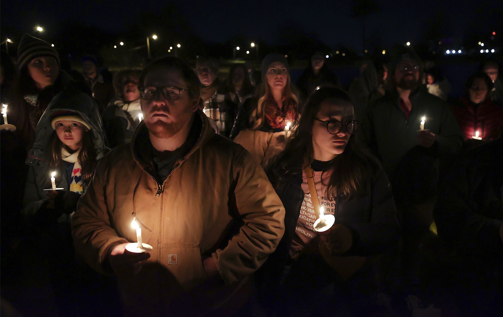 A crowd of somber people holding candles as they stand outside in the dark