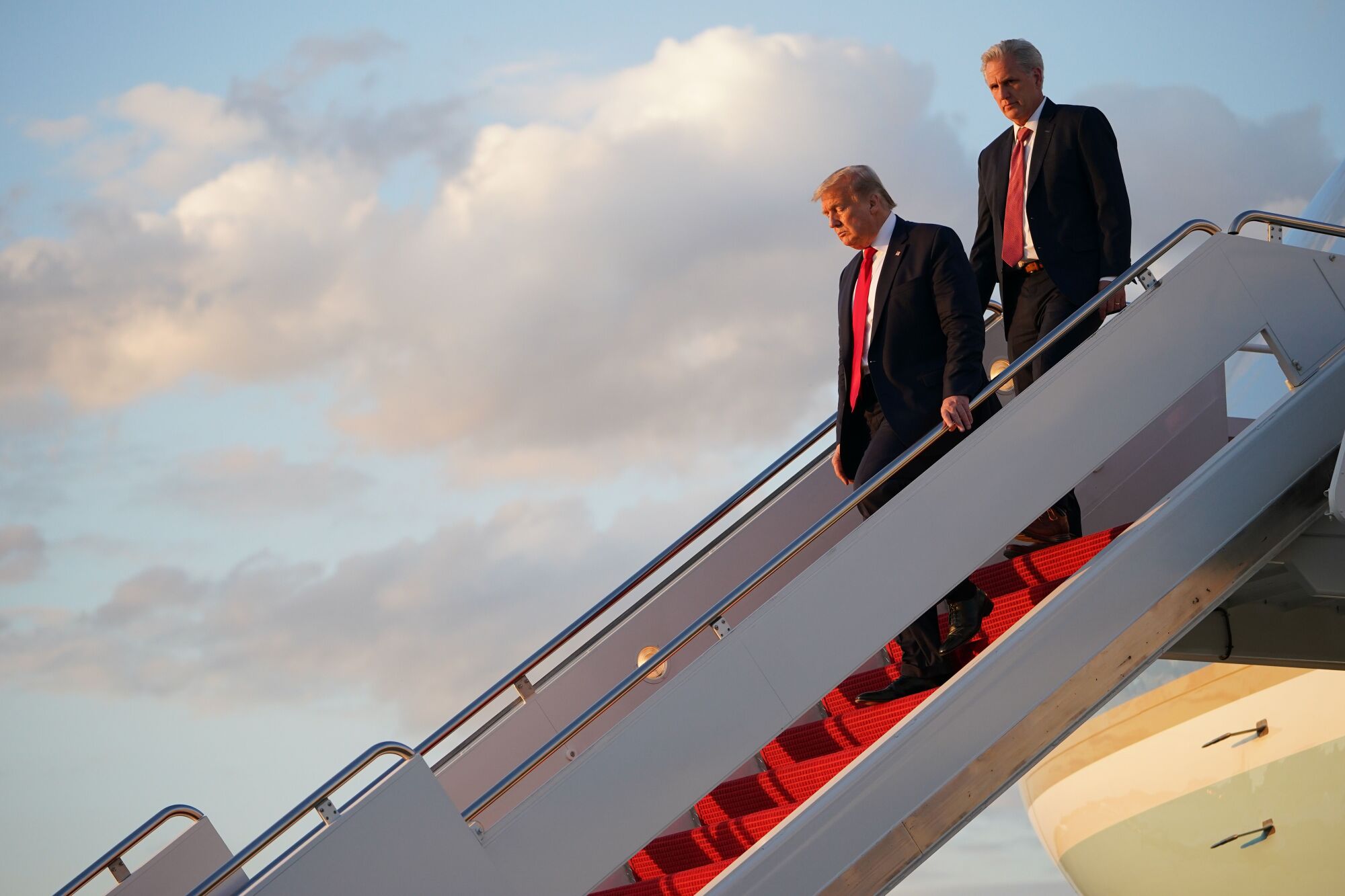 Two men walk down steps from a plane.