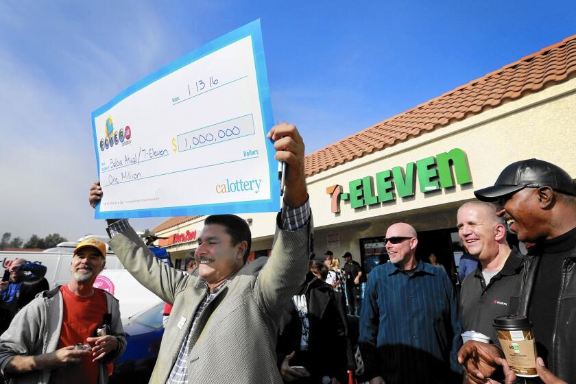 Balbir Atwal, owner of the 7-Eleven store in Chino Hills that sold a winning Powerball ticket, holds up an oversized prop check for $1 million, the business’ take for selling one of the three tickets that won the $1.5-billion jackpot.