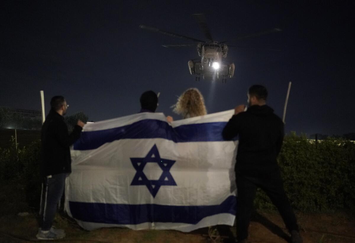  People holding a blue-and-white flag with a blue star watch the arrival of a helicopter