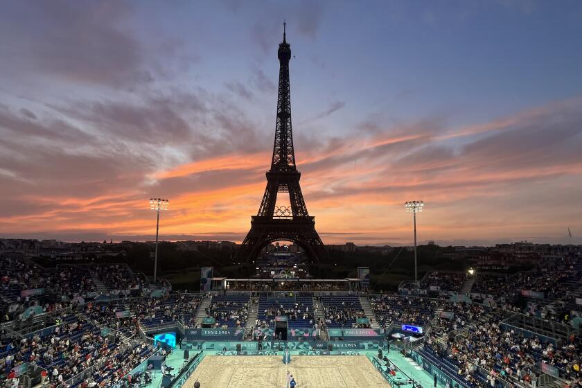 Spectators photograph a colorful sunset at Eiffel Tower Stadium prior to a beach volleyball match.